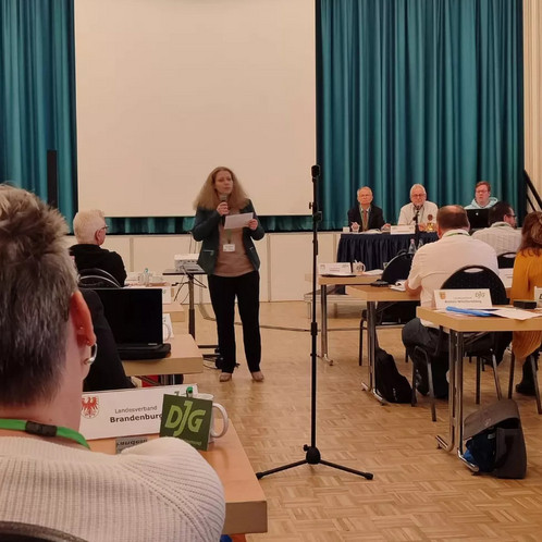 Bianca Korbanek auf dem DJG Bundesgewerkschaftstag 2023 Eine Frau steht in der Mitte eines Seminarraums und spricht vor den anderen Anwesenden in ein Mikrofon