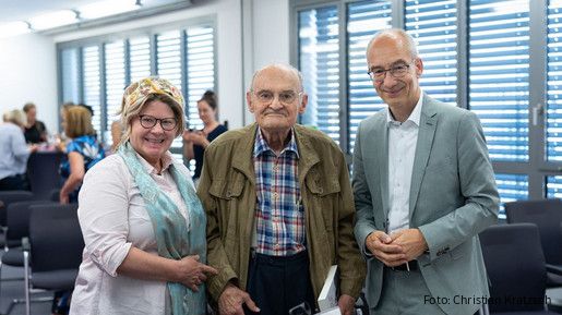 Drei Menschen stehen in einem Tagungsraum und blicken in die Kamera