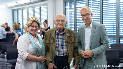 Drei Menschen stehen in einem Tagungsraum und blicken in die Kamera