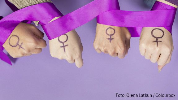 Der Feminismus in Deutschland ist zunehmenden Angriffen ausgesetzt Vier Frauenhände mit einem aufgemalten Frauen-Symbol, ein violettes Band ist um die Handgelenke gelegt