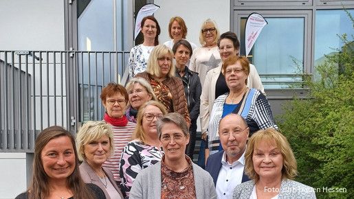 Eine Gruppe Menschen steht auf einer Treppe vor einem Haus und schaut in die Kamera.